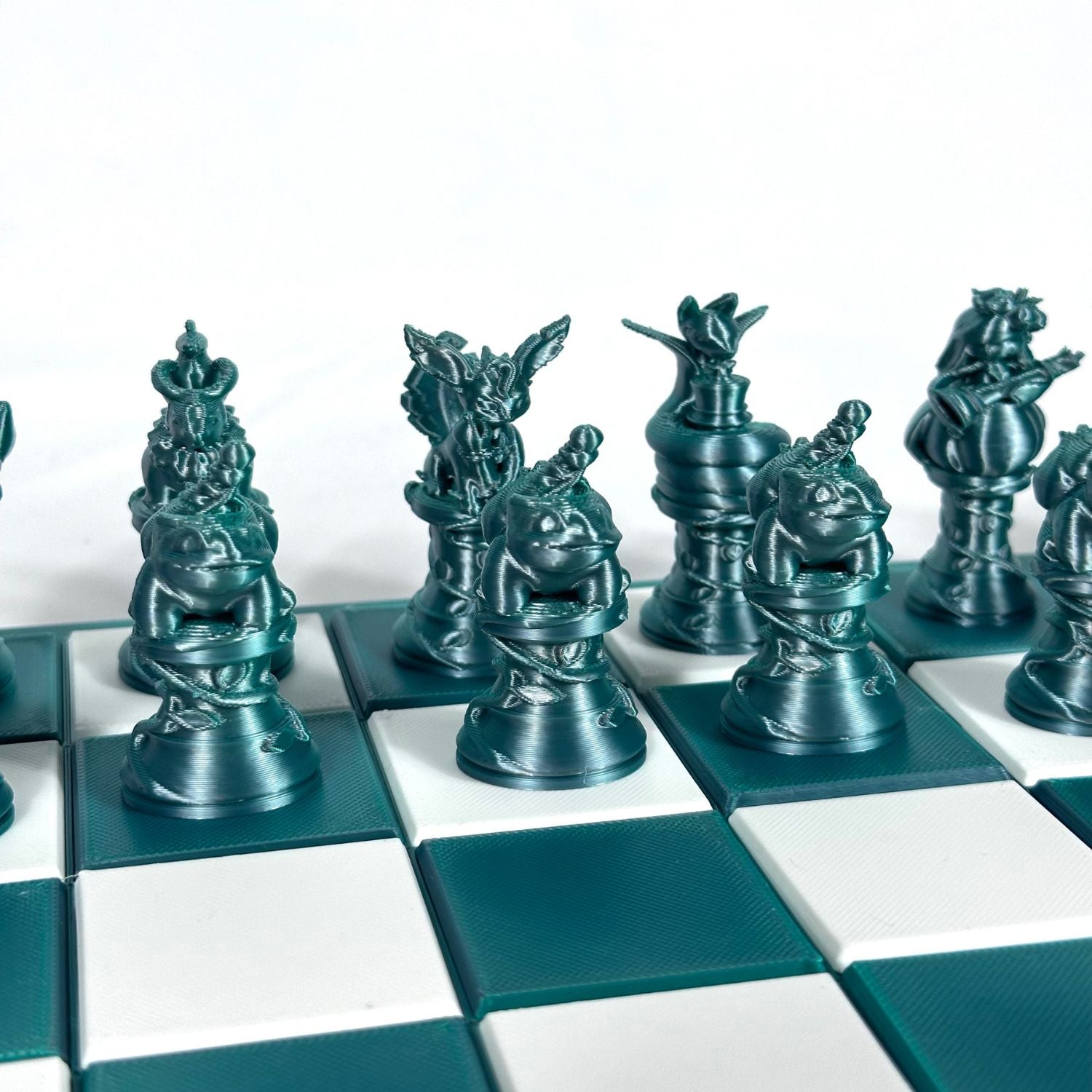 Set d’échecs Pokémon jade chromé avec pièces détaillées et stylisées, alignées sur un plateau vert et blanc.