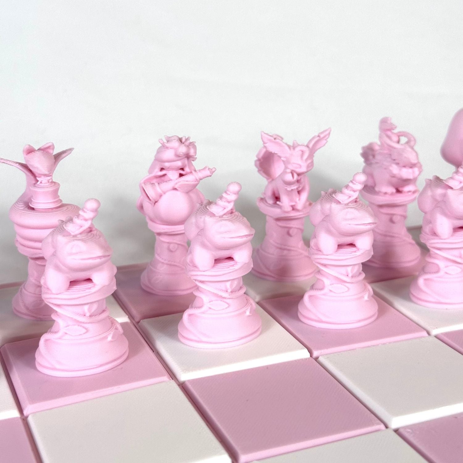 Gros plan sur les pièces d’échecs Pokémon couleur rose pastel, imprimées en 3D avec un design détaillé.