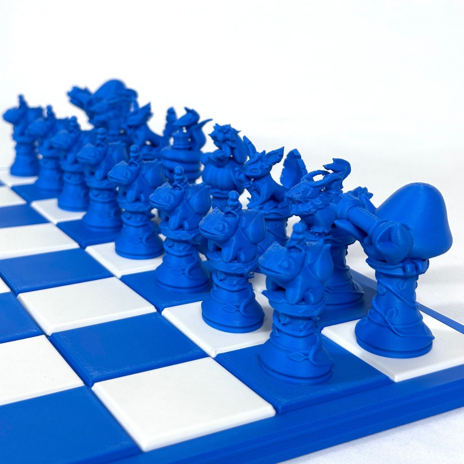 Pièces d’échecs fantasy style Pokémon en impression 3D bleu saphir, vues en gros plan sur échiquier.