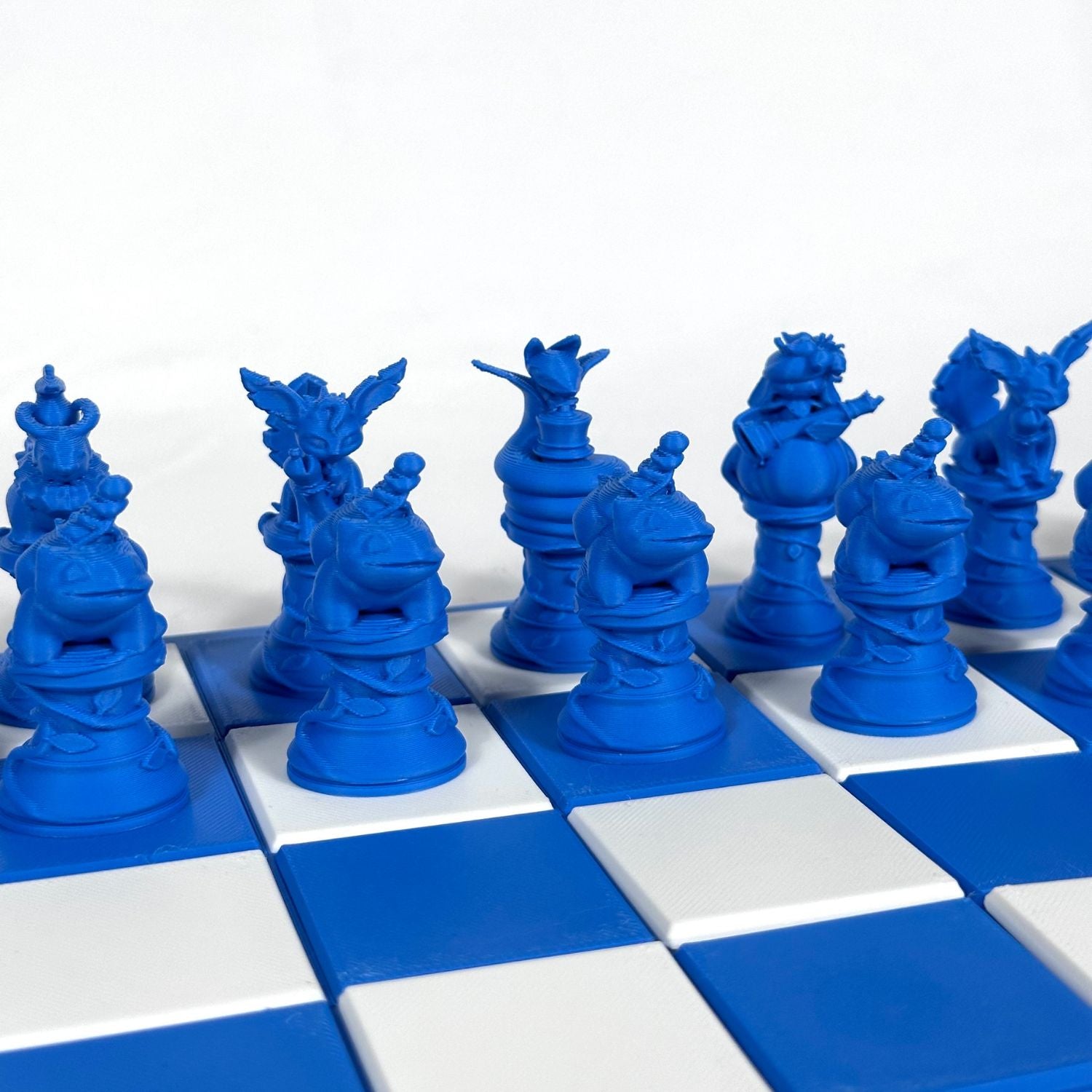 Set d’échecs Pokémon bleu saphir avec pièces détaillées, stylisées et disposées sur un plateau quadrillé bleu et blanc.