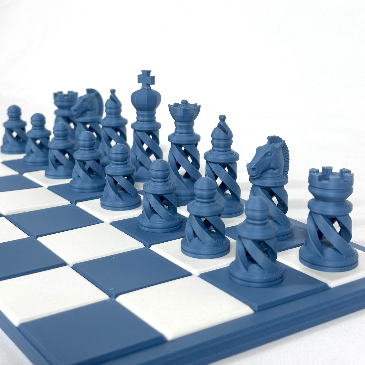 Pièces d’échecs imprimées en 3D de couleur bleu acier, style moderne ajouré, alignées sur un échiquier bleu et blanc.