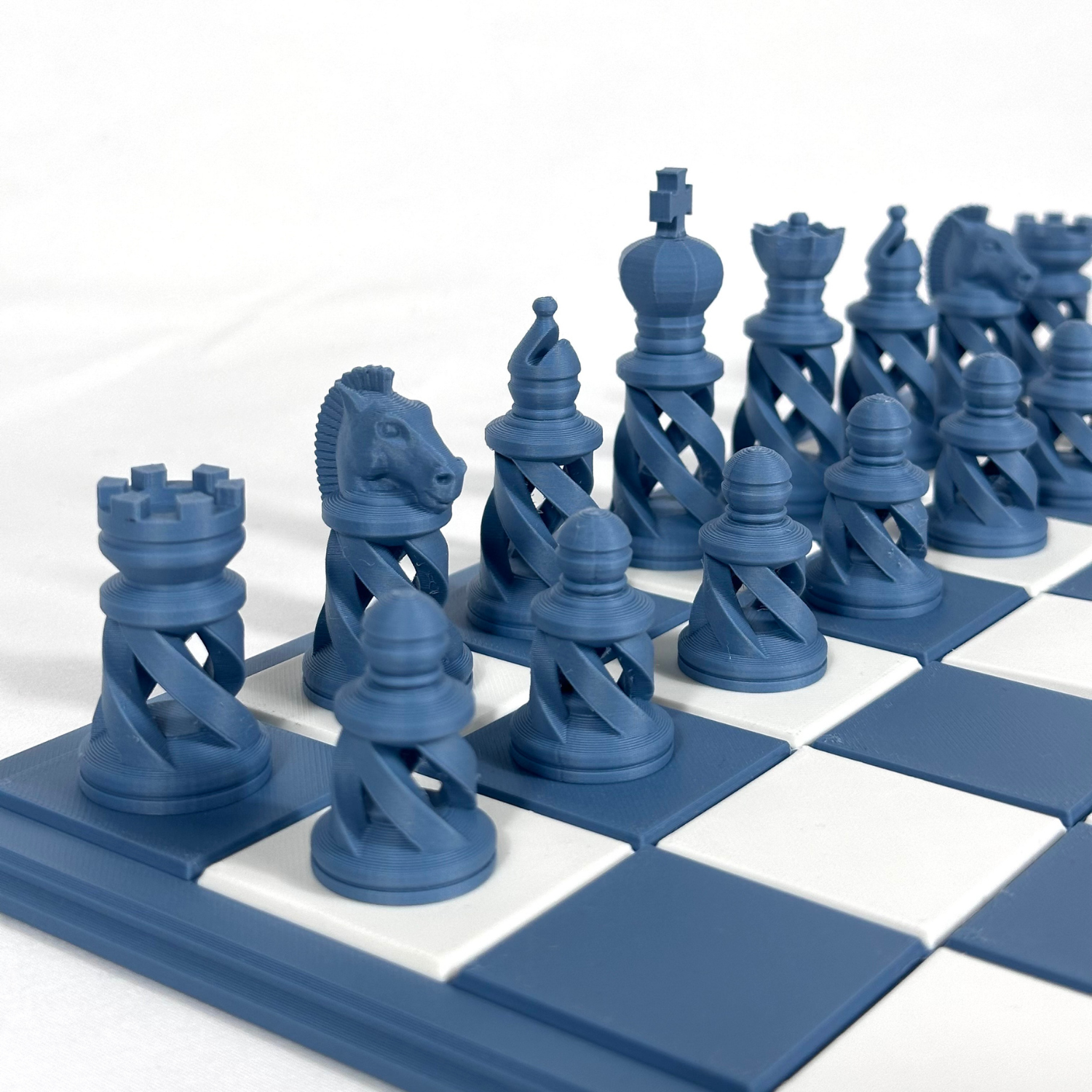 Jeu d’échecs moderne bleu avec pièces ajourées en spirale, imprimées en 3D, disposées sur un échiquier bleu et blanc.