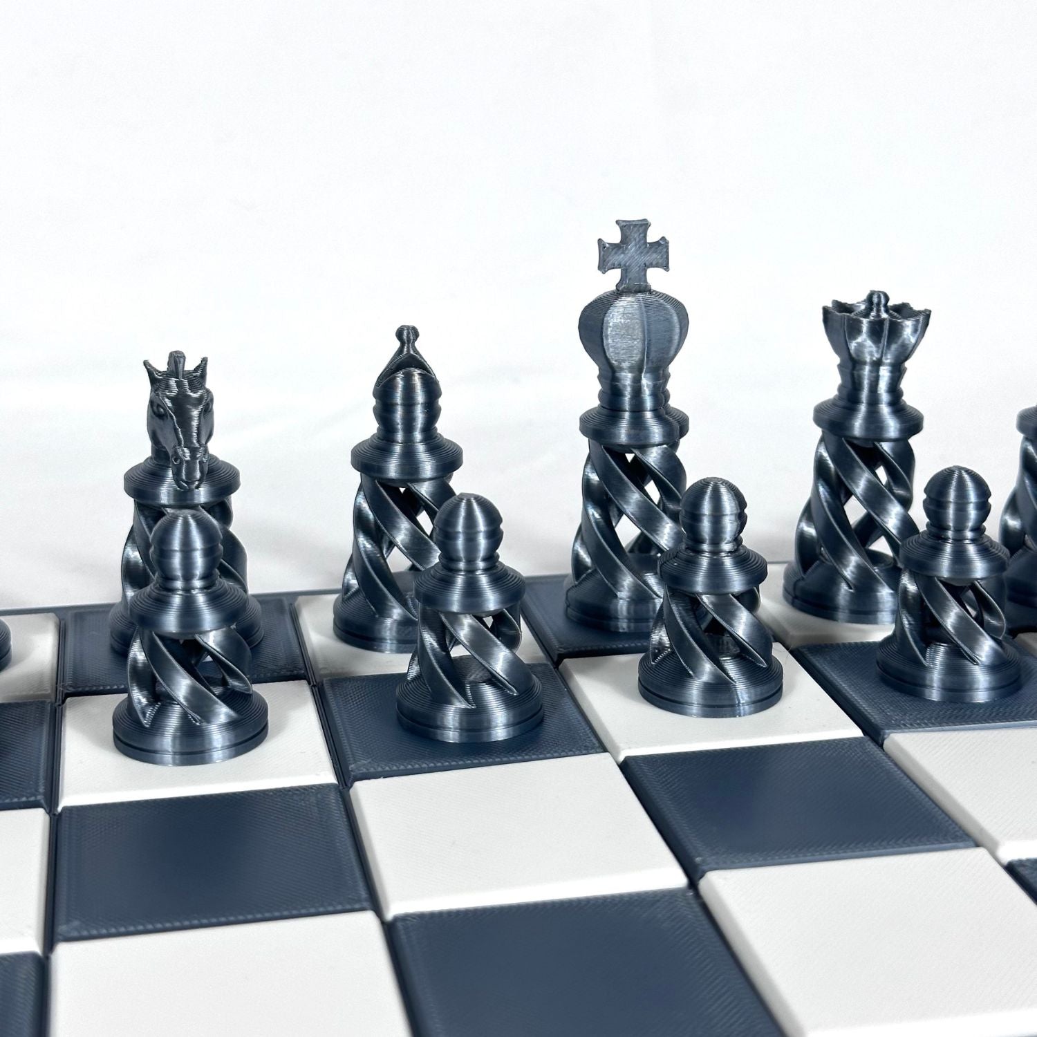 Jeu d’échecs gris métallisé avec finition spiralée design, cavaliers et tours visibles sur plateau contrasté.