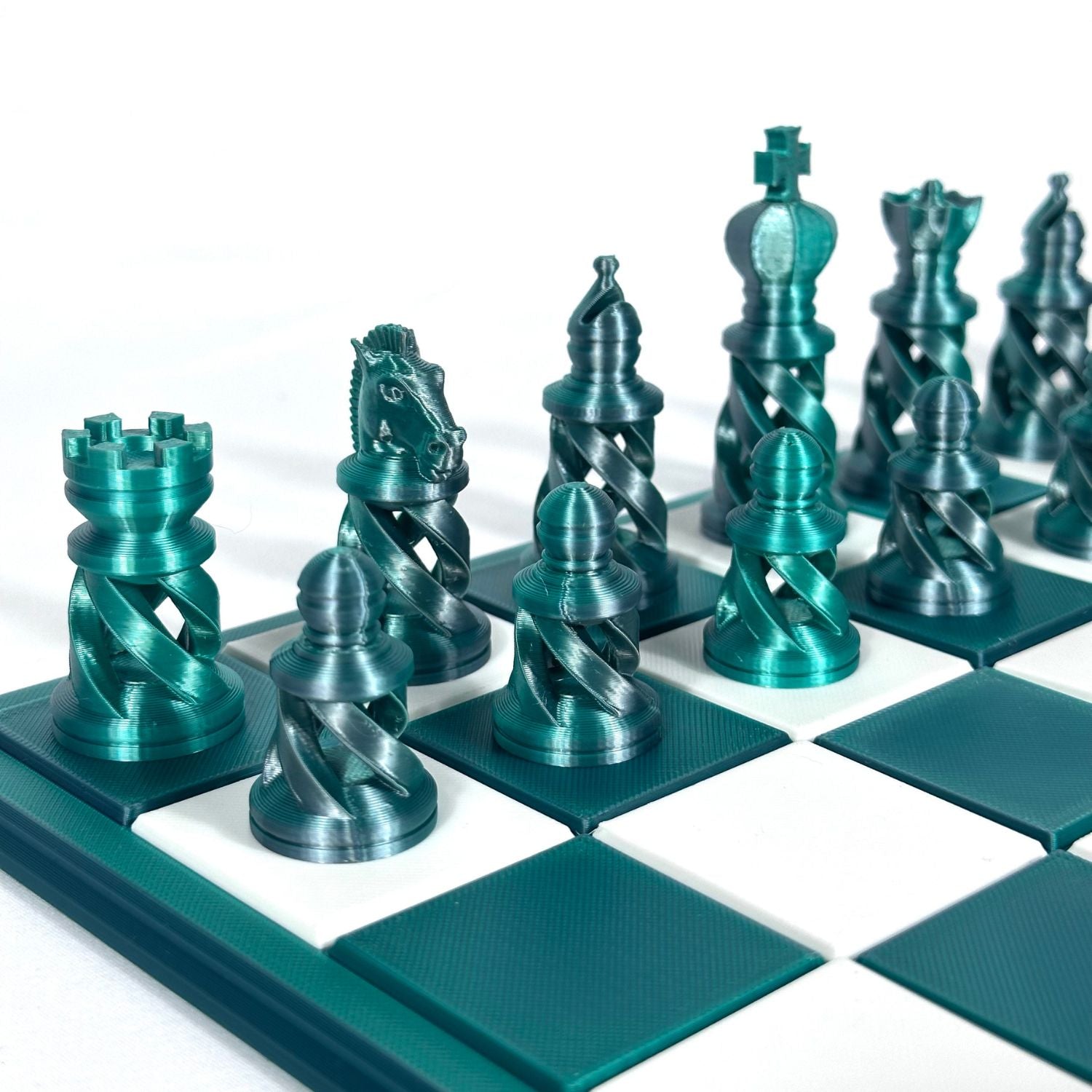 Pièces d’échecs modernes coloris jade et chrome, design spiralé imprimé en 3D, sur plateau blanc et vert foncé.