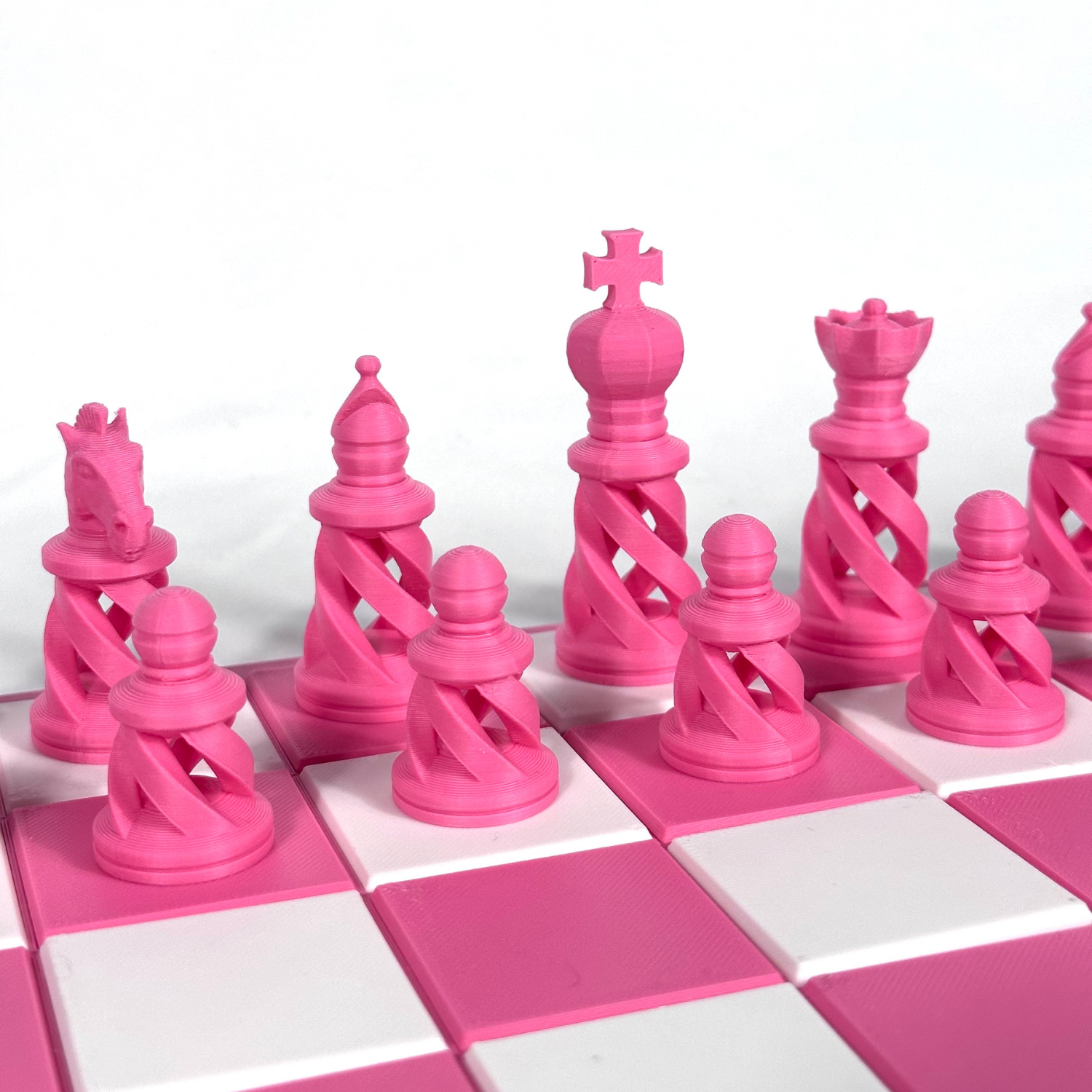 Jeu d’échecs rose avec pièces stylisées en spirale, imprimées en 3D, alignées sur un plateau rose et blanc.