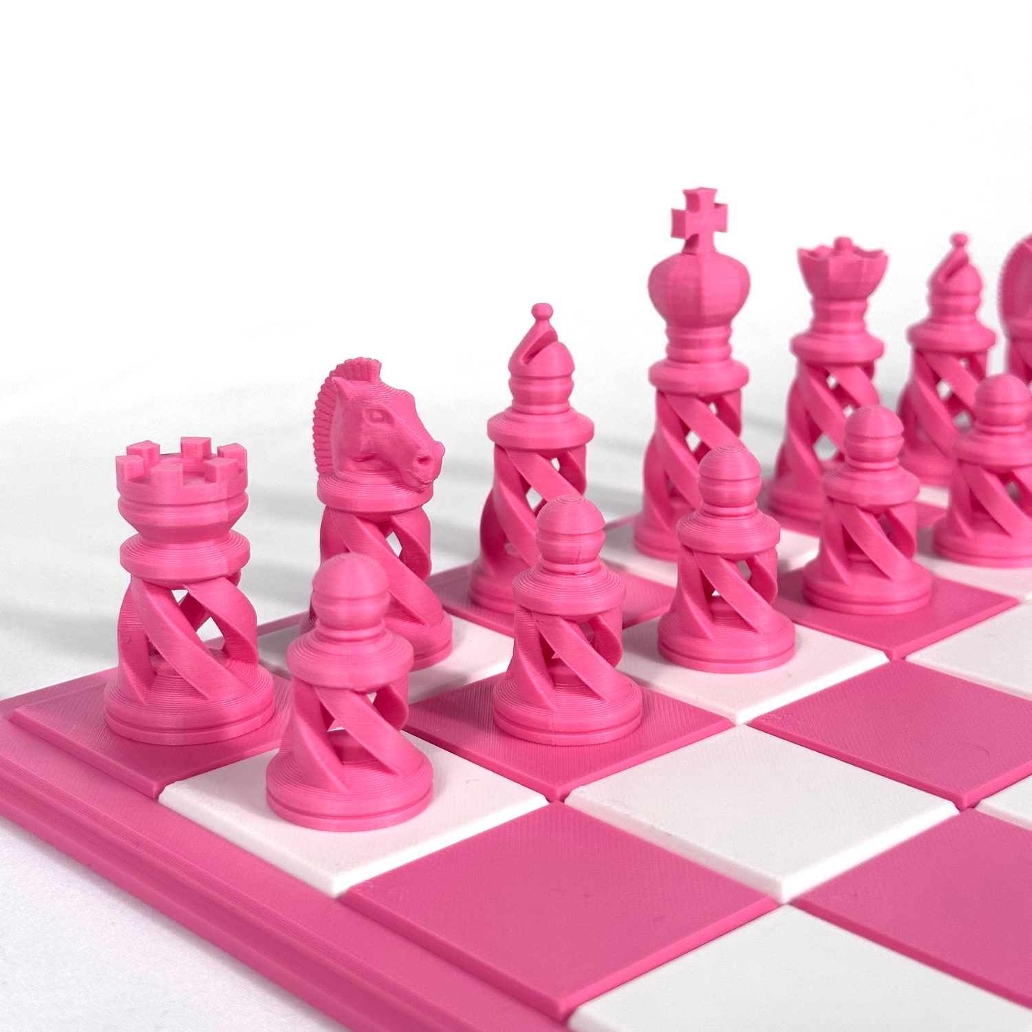 Pièces d’échecs modernes roses, imprimées en 3D avec design ajouré en spirale, disposées sur un échiquier rose et blanc.