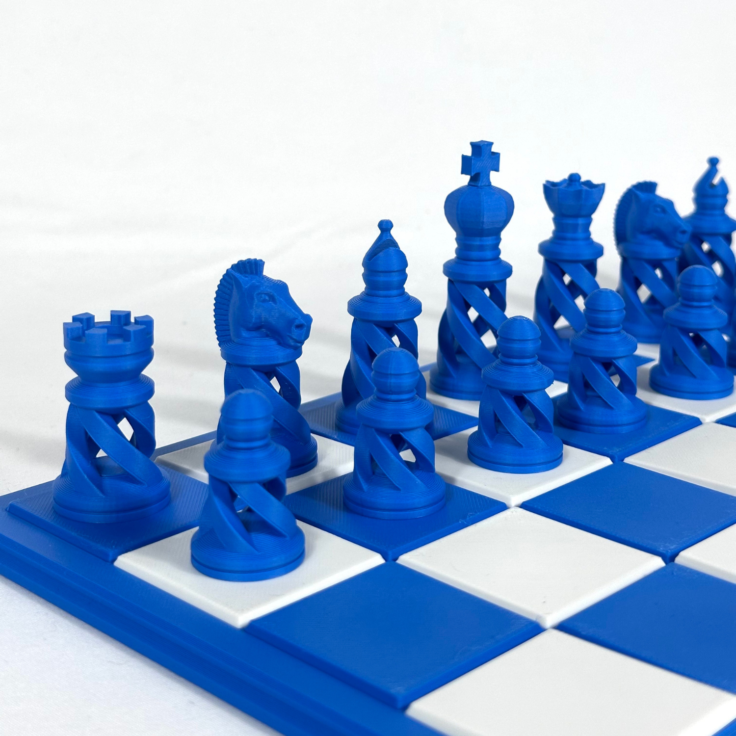 Jeu d’échecs moderne couleur bleu saphir, pièces spiralées imprimées en 3D, sur plateau blanc et bleu.