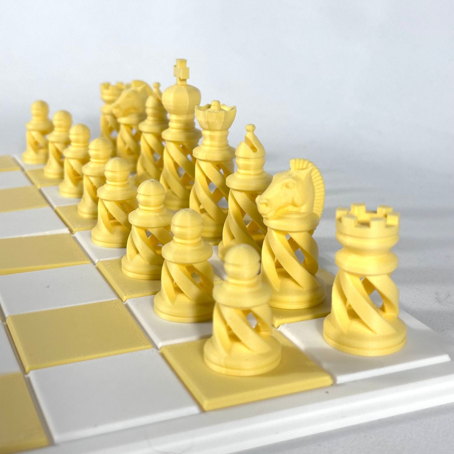 Set d’échecs moderne imprimé en 3D, teinte jaune clair, design spiralé sur échiquier stylisé.