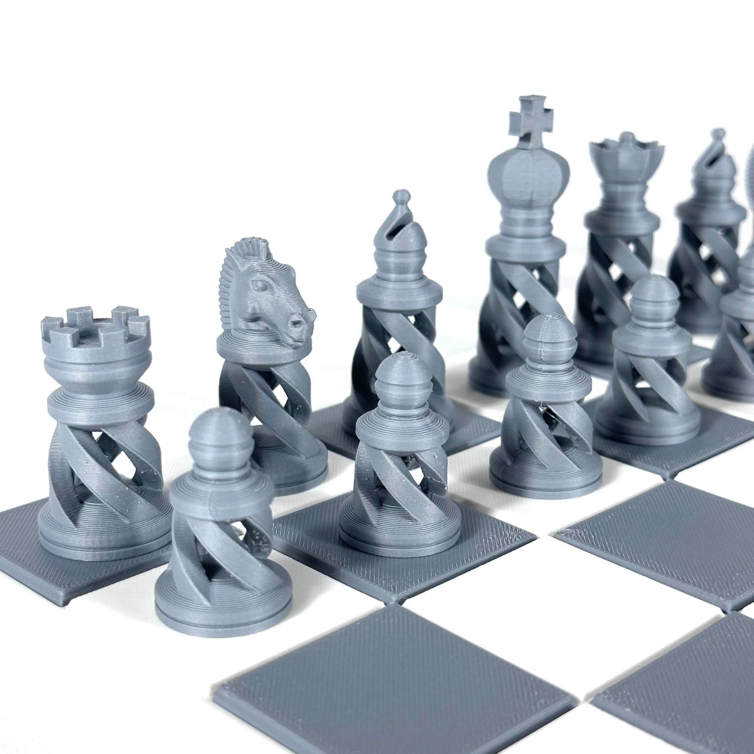 Pièces d’échecs modernes couleur gris métallisé sur plateau gris et blanc, design spiralé imprimé en 3D.
