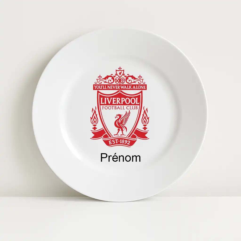 Assiette blanche incassable arborant le logo emblématique du Liverpool Football Club en rouge vif. L'inscription "You'll Never Walk Alone" est visible en haut du blason, avec "Prénom" écrit en dessous pour une personnalisation.