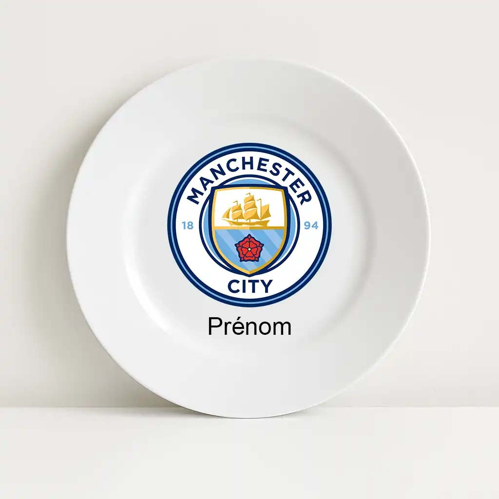 Assiette blanche incassable avec le logo du club Manchester City au centre. Le blason bleu et doré représente un navire doré, une rose rouge et les dates "1894". Sous le logo, l'inscription "Prénom" est prévue pour la personnalisation.