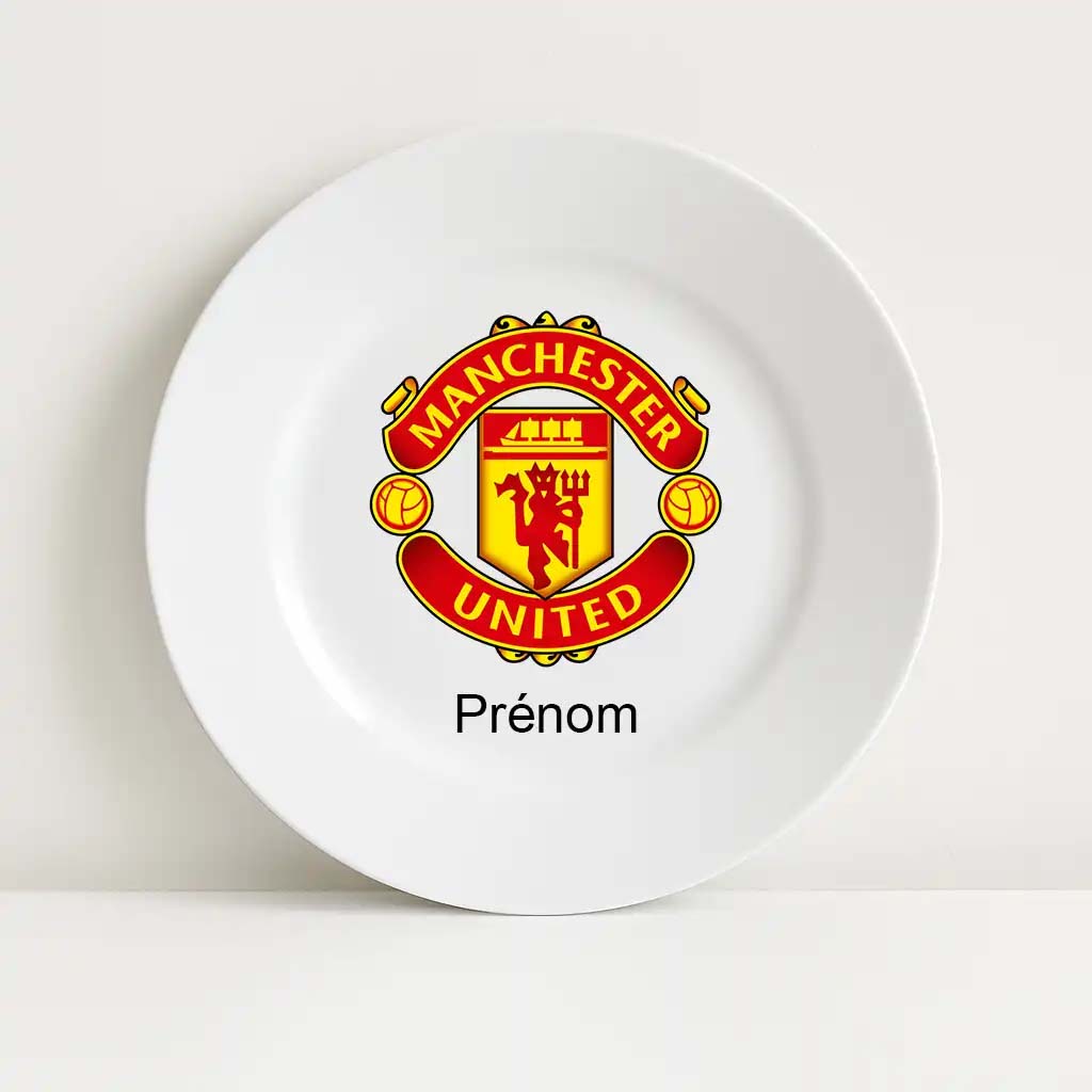 Assiette blanche incassable avec le logo du club Manchester United au centre. Le blason rouge et jaune affiche un diable tenant une fourche, entouré de deux ballons. En dessous, l’inscription "Prénom" est prévue pour la personnalisation.