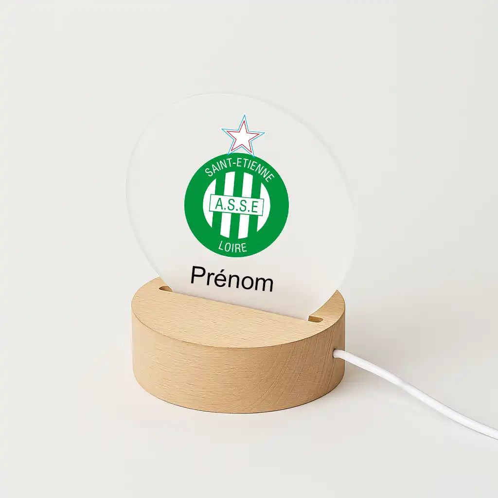 Lampe LED personnalisable avec le logo de L'AS Saint-Etienne, posée sur une base en bois clair, avec l'inscription "Prénom" sous l'écusson du club.