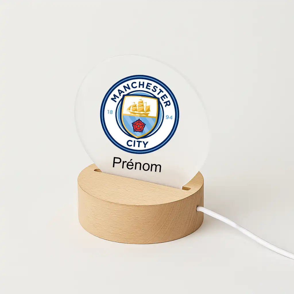 Lampe LED personnalisable avec le logo de Manchester City, posée sur une base en bois clair, avec l'inscription "Prénom" sous l'écusson du club.