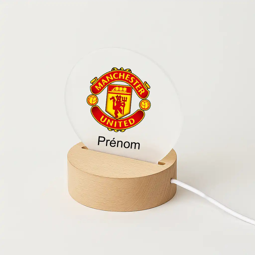 Lampe LED personnalisable avec le logo de Manchester United, posée sur une base en bois clair, avec l'inscription "Prénom" sous l'écusson du club.
