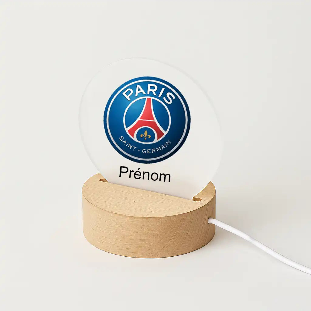 Lampe LED personnalisable avec le logo du Paris Saint Germain, posée sur une base en bois clair, avec l'inscription "Prénom" sous l'écusson du club.