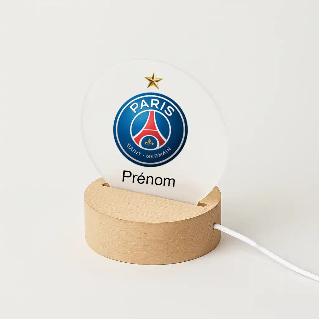 Lampe LED personnalisable avec le logo du PSG avec 1 étoile, posée sur une base en bois clair, avec l'inscription "Prénom" sous l'écusson du club.
