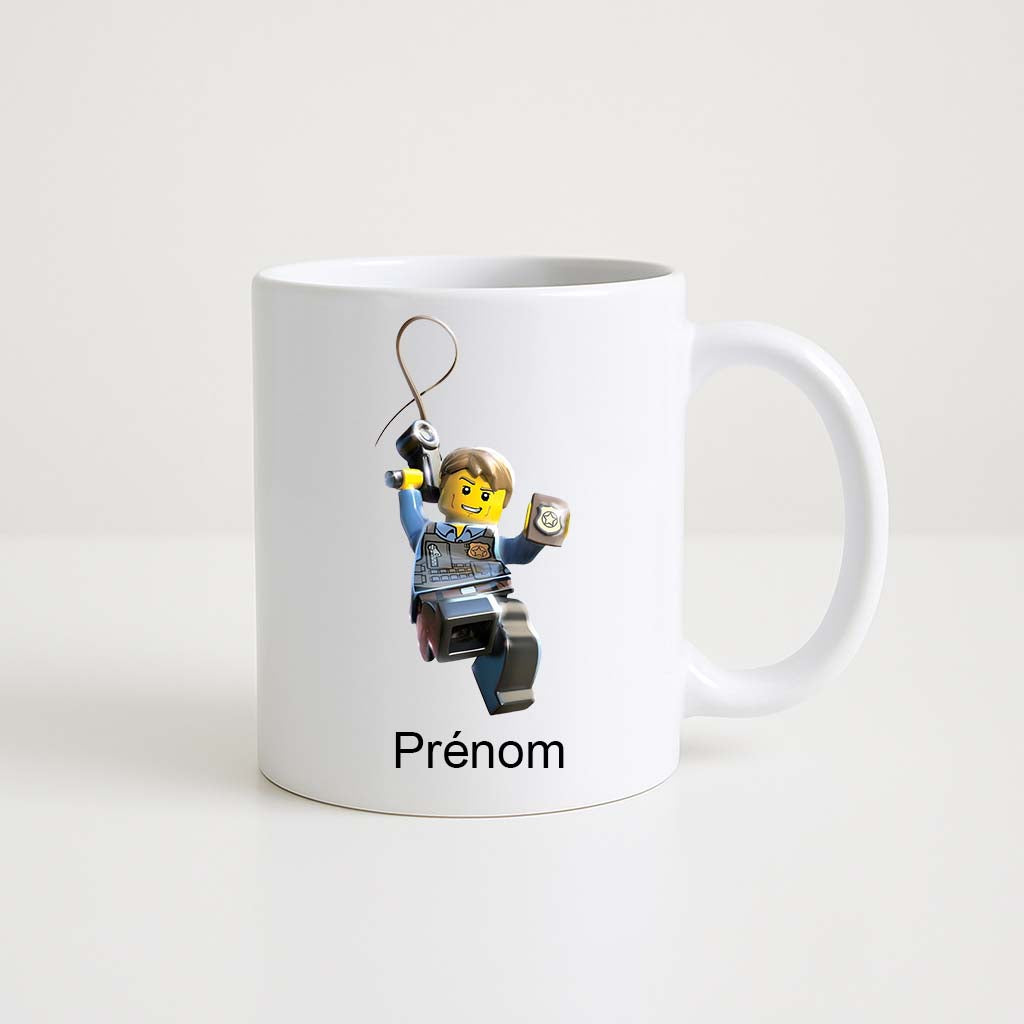 Mug blanc 330 ml avec illustration d’un policier Lego suspendu à une corde, personnalisable avec un prénom.
