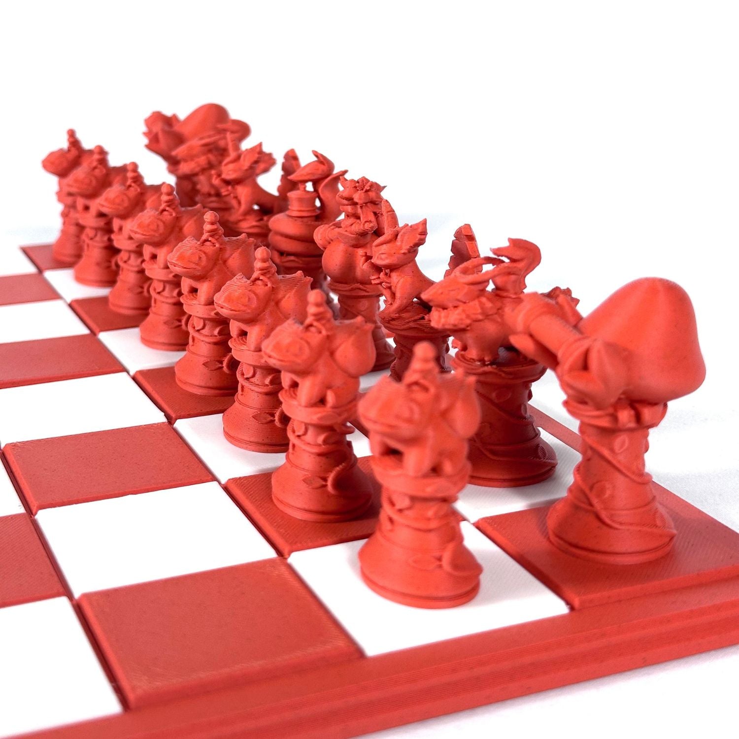 Gros plan sur les pièces d’échecs Pokémon imprimées en 3D, couleur brique, posées sur un échiquier rouge et blanc moderne.