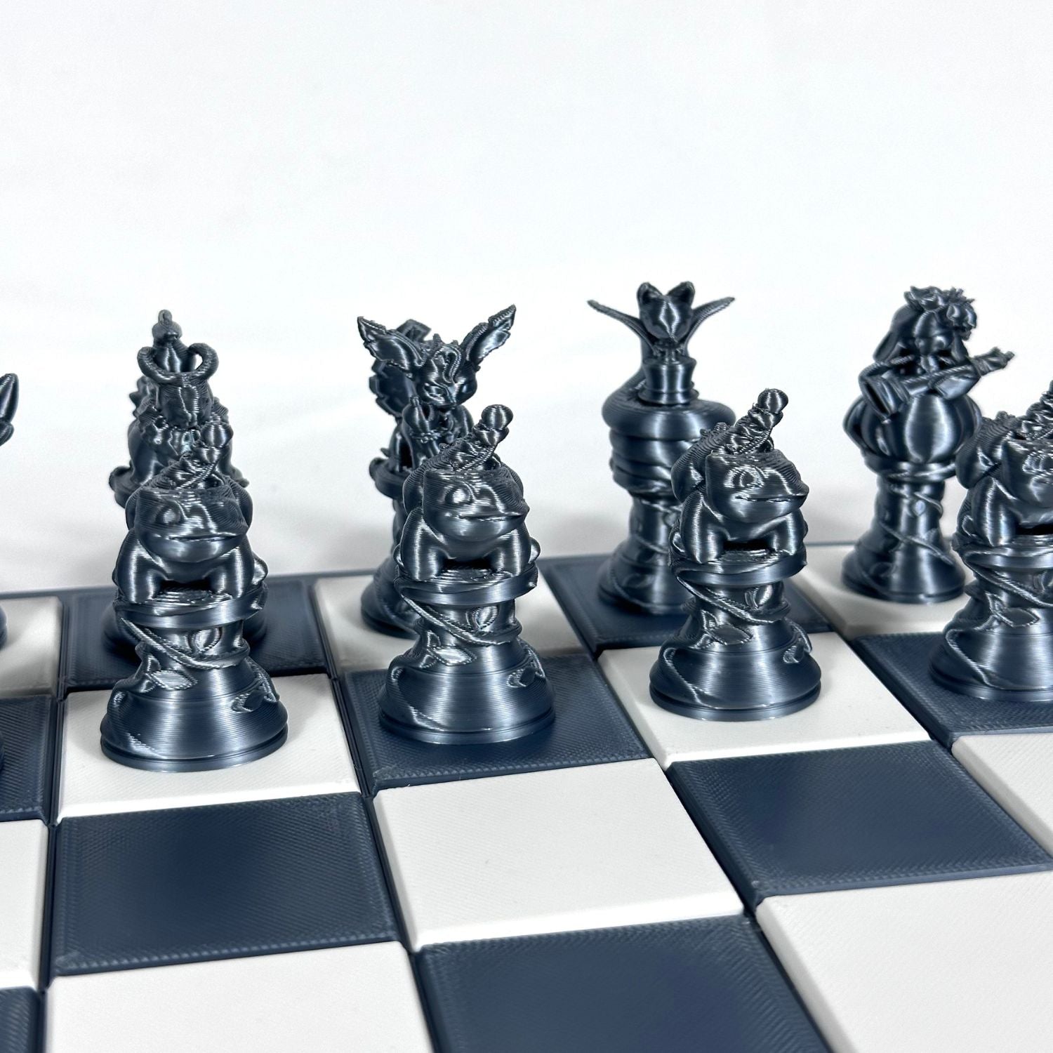 Set d’échecs Pokémon chromé sombre avec pièces détaillées et stylisées, disposé sur un plateau quadrillé bleu foncé et blanc.