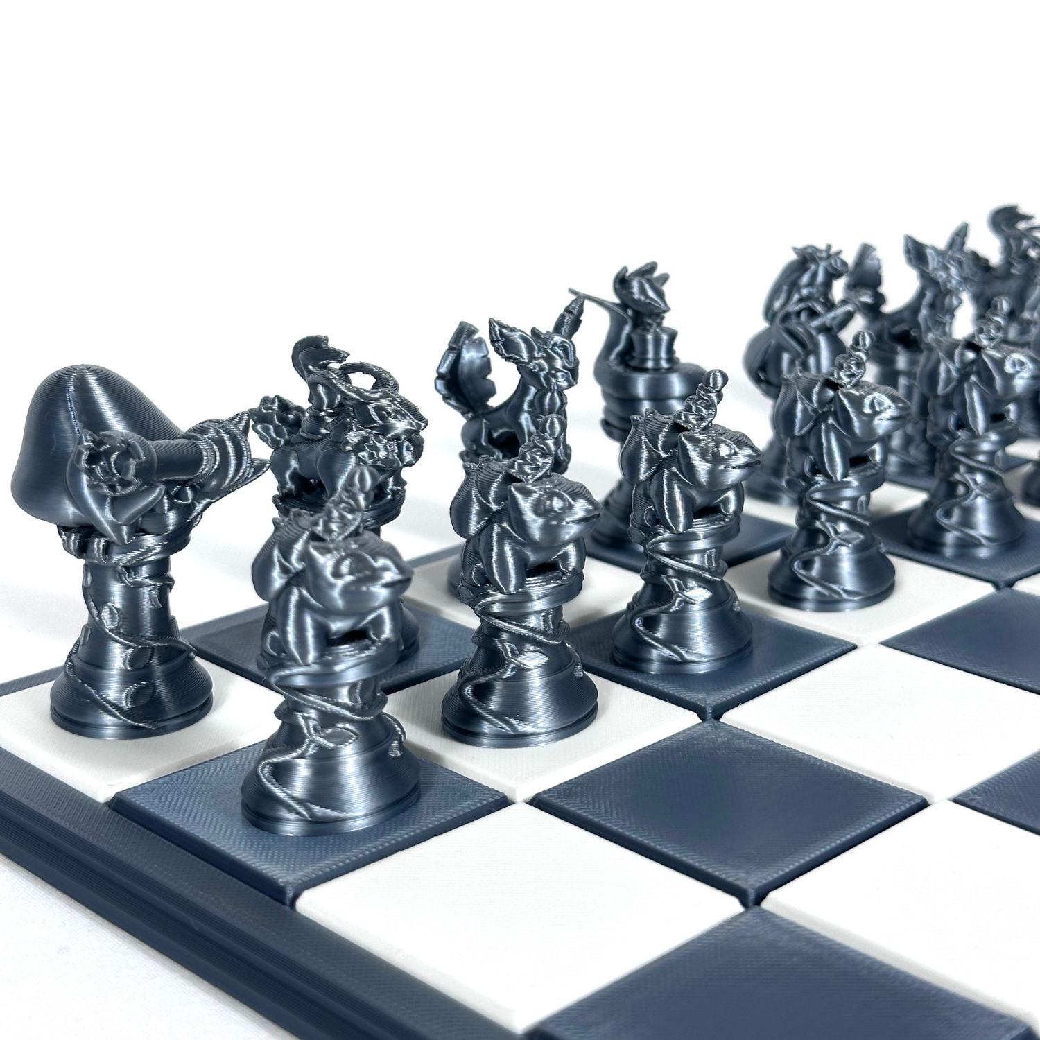 Pièces d’échecs Pokémon finition chrome sombre imprimées en 3D, alignées sur un échiquier bleu foncé et blanc.