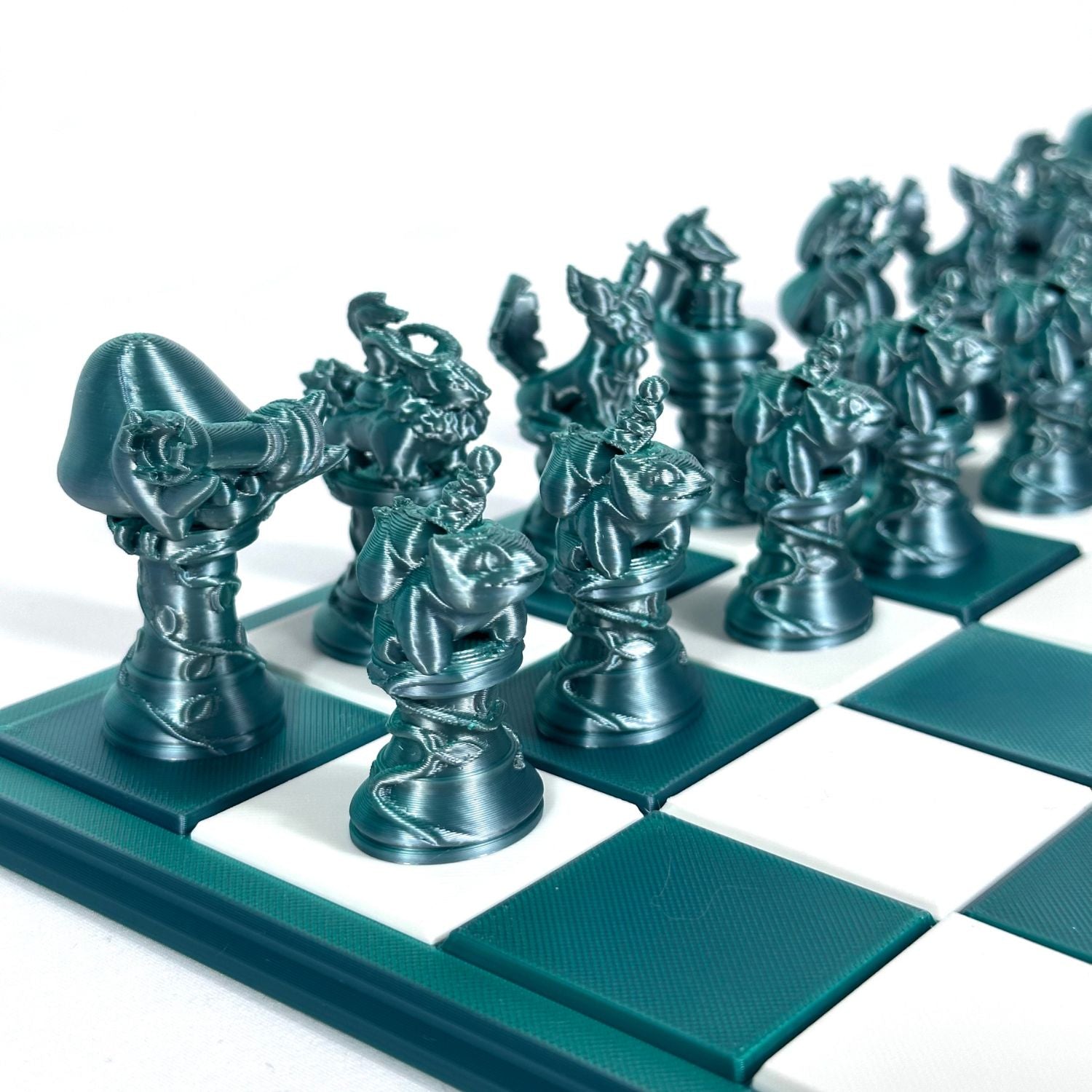 Pièces d’échecs inspirées Pokémon en finition jade chromé, imprimées en 3D et disposées sur un échiquier vert et blanc.