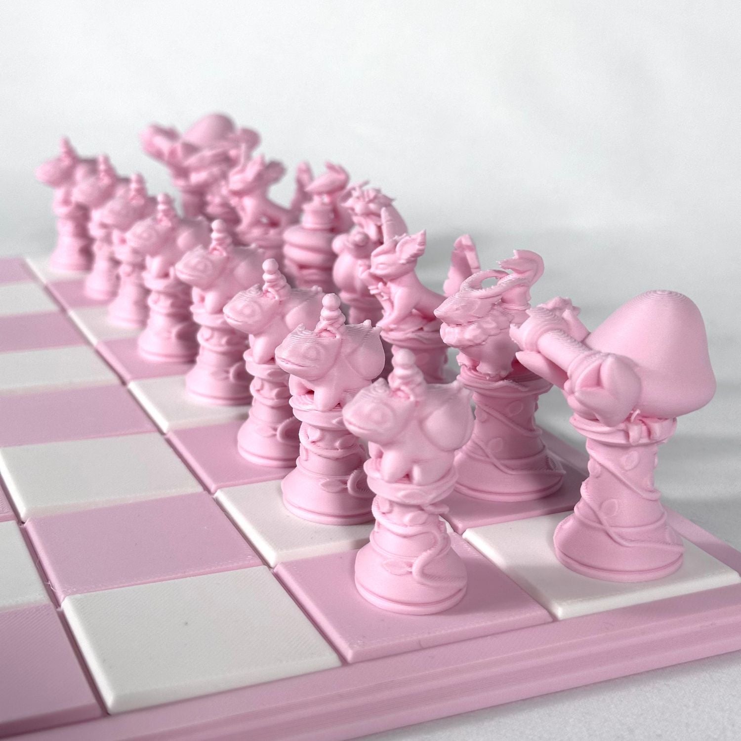Ensemble complet de pièces d’échecs Pokémon 3D couleur rose pastel disposées sur un échiquier rose et blanc.