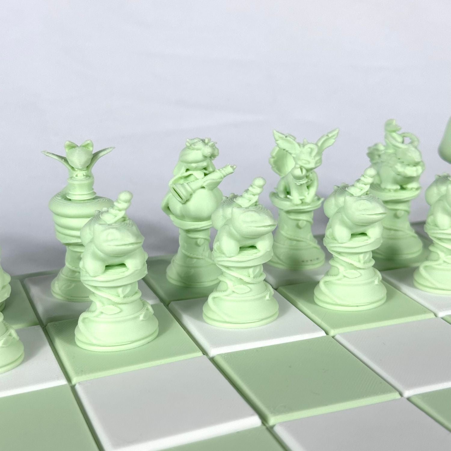 Gros plan sur les pièces d’échecs Pokémon imprimées en 3D couleur vert pastel, au design détaillé.