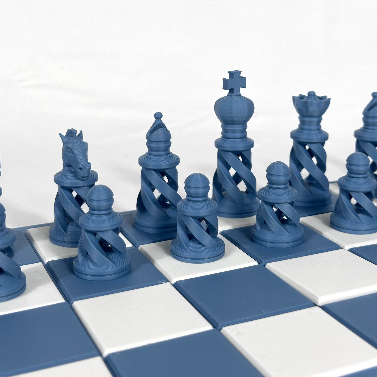 Pièces d’échecs bleues au design ajouré en spirale sur un plateau bleu et blanc, vue rapprochée sur les pions, cavaliers et pièces majeures.