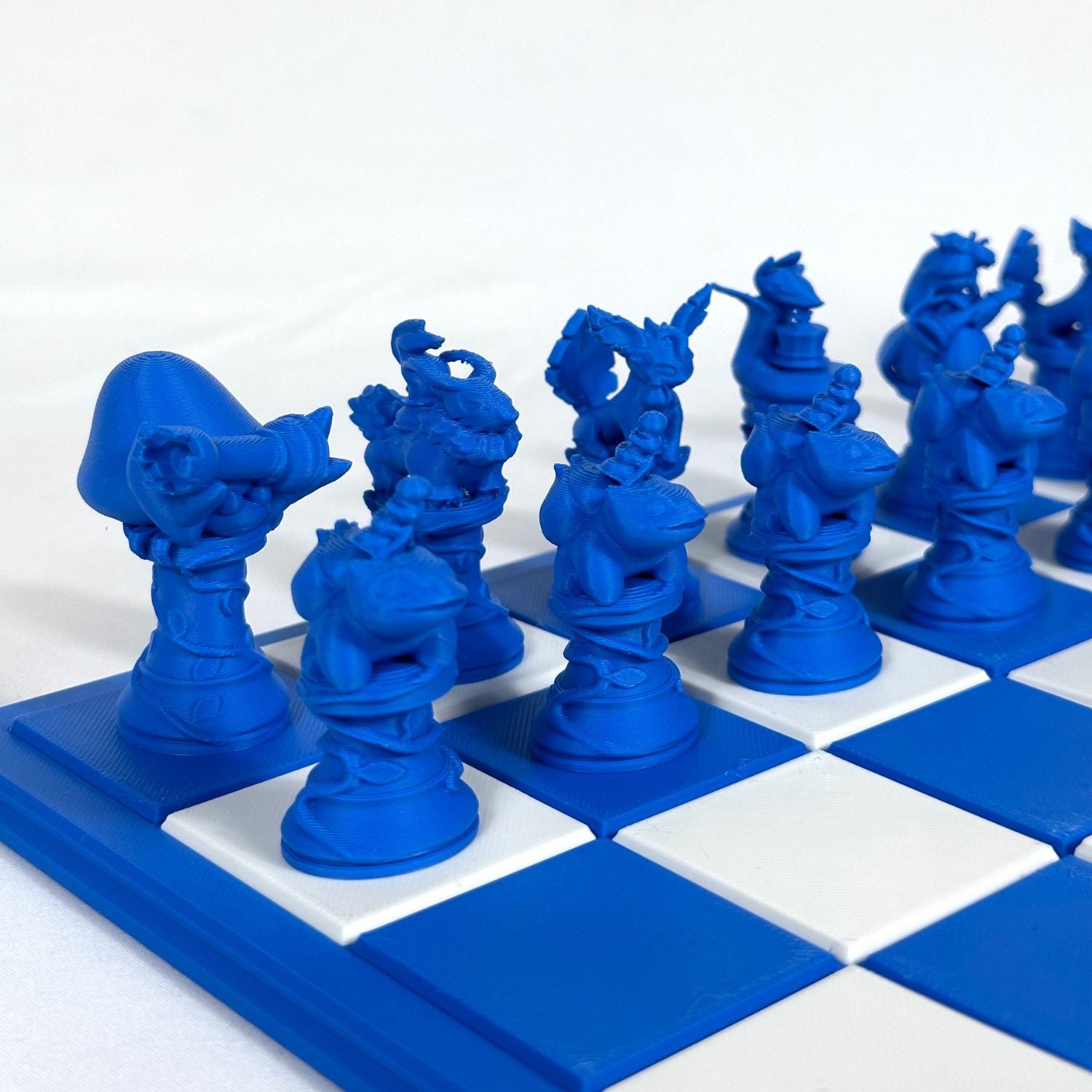 Pièces d’échecs inspirées Pokémon en bleu saphir, imprimées en 3D et alignées sur un échiquier bleu et blanc.